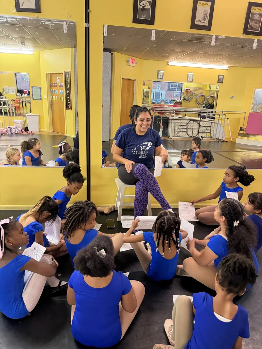 A teacher leading a Rising Star Institute lesson with dancers seated around her holding worksheets