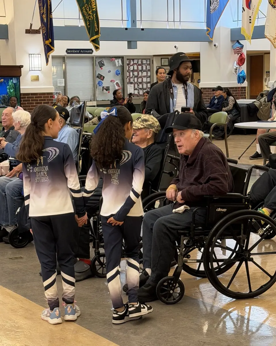 Two dancers in American Dance Studios team suits greeting veterans in wheelchairs at the veterans hospital