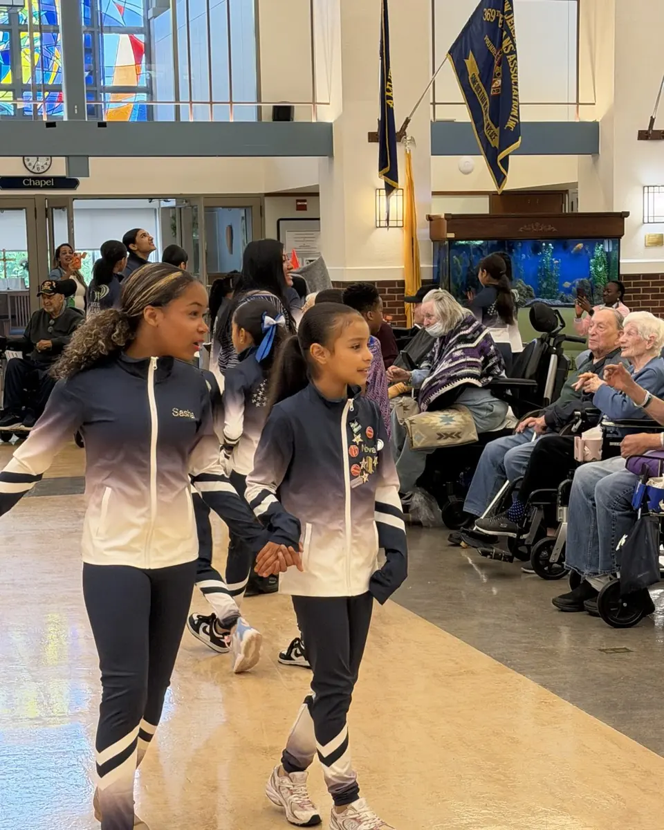 An older dancer holding a younger dancer's hand as they walk past residents at the veterans hospital